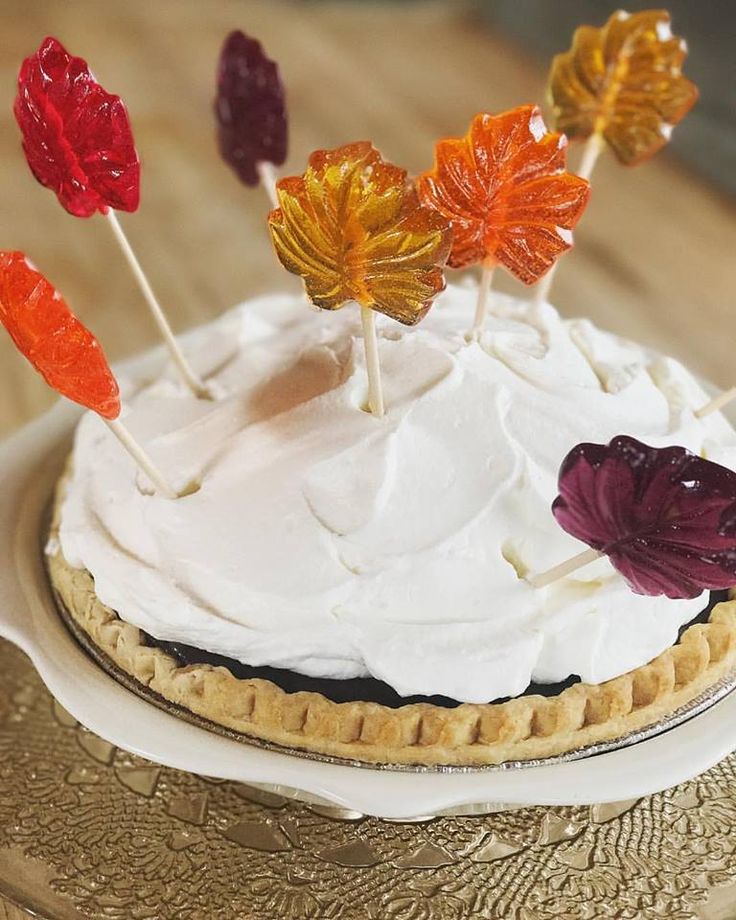 a pie with white frosting and colorful leaf decorations on it's top, sitting on a table