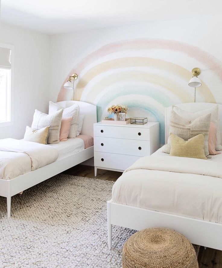 two white beds in a bedroom with a rainbow painted wall behind them and a rug on the floor