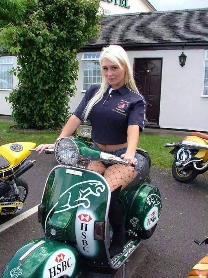 a woman riding on the back of a green scooter in a parking lot