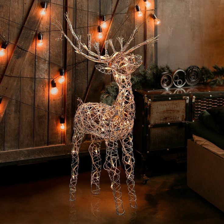 a lighted deer standing in front of a wooden wall with christmas lights on it's antlers