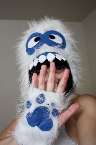 a person wearing a furry animal mask and holding their hands up to their face with one hand