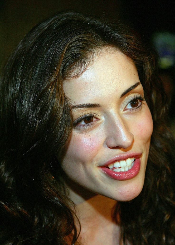 a close up of a woman with long dark hair smiling at the camera and holding a cell phone to her ear