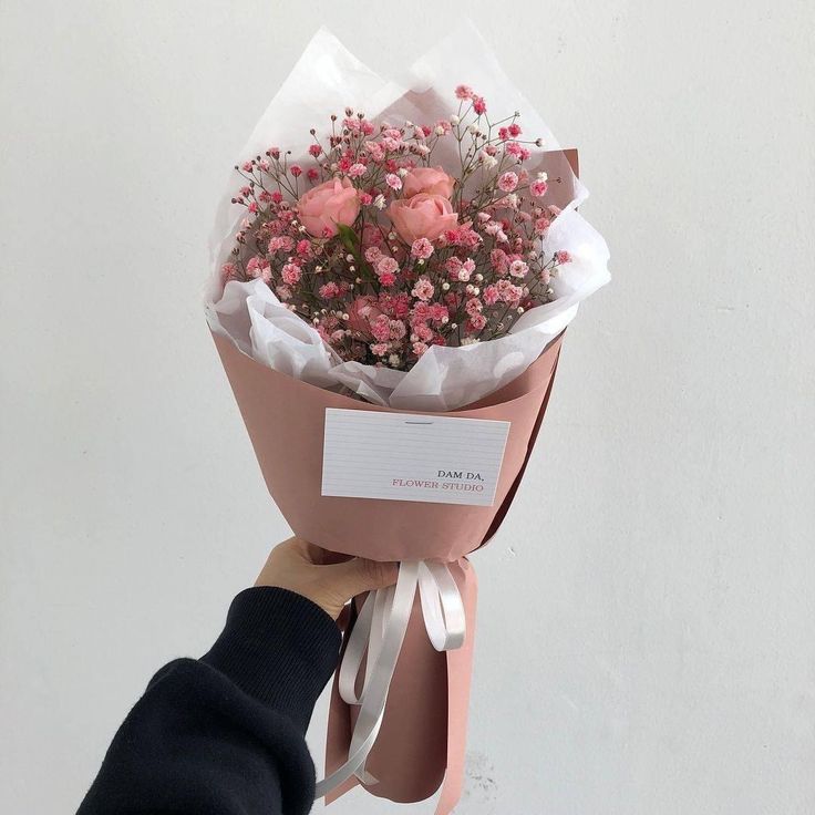 a person holding a bouquet of flowers in their hand with a note attached to it