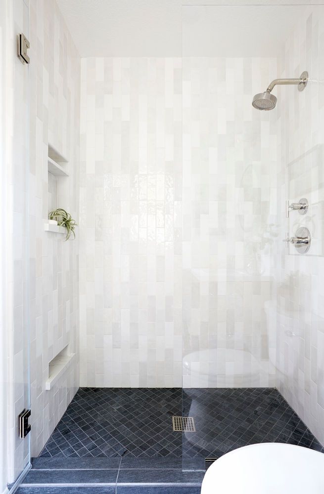 a white tiled bathroom with black tile flooring and shower head mounted to the wall