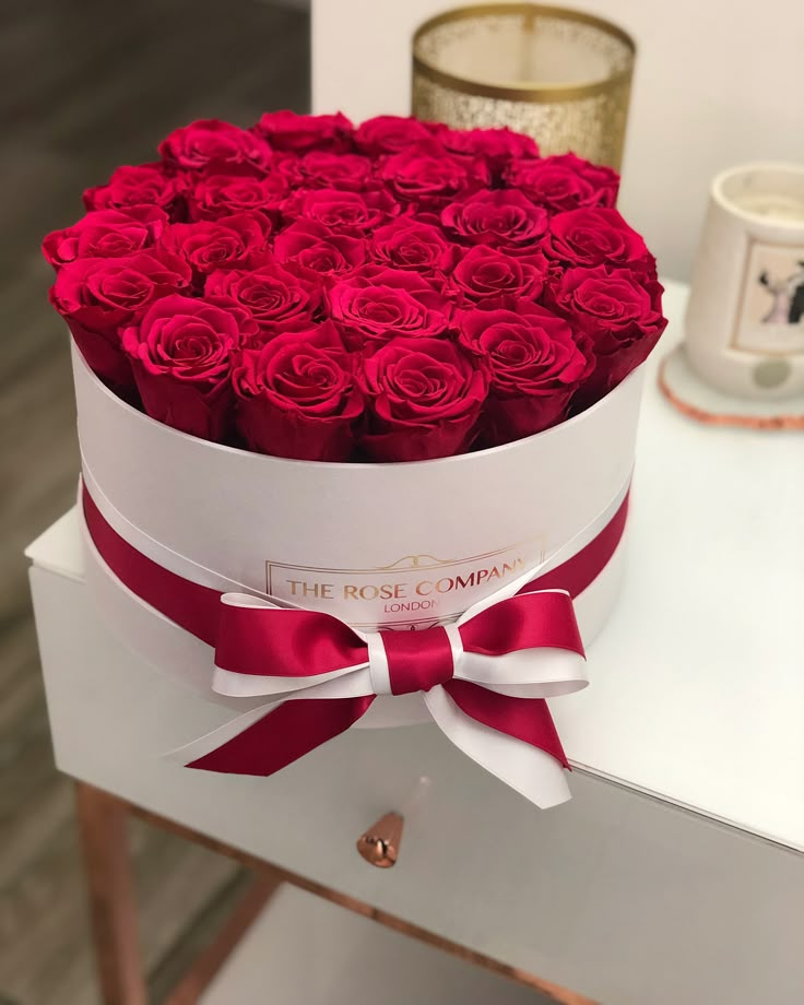 a white box filled with red roses on top of a table