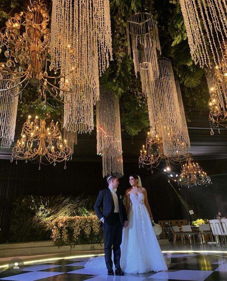 a bride and groom are standing under chandeliers