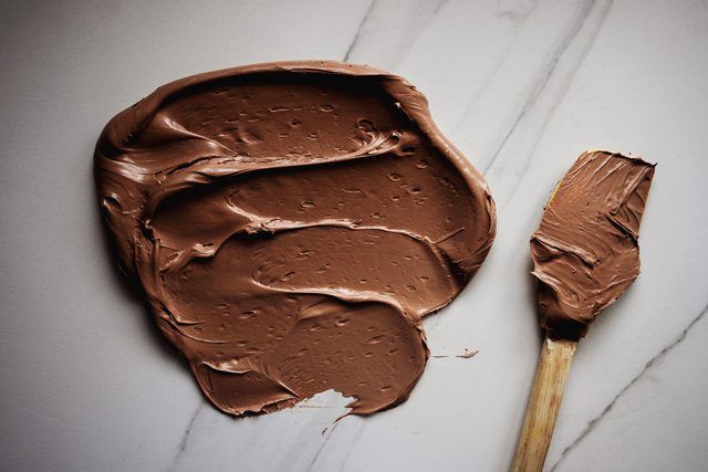 a spoon with chocolate on it next to a paintbrush and some brown stuff in the background