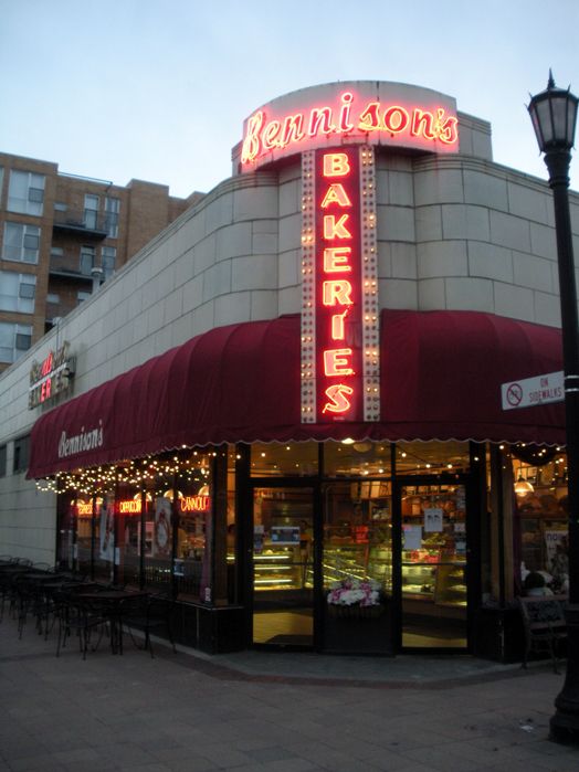 the front of a restaurant with lights on it's windows and red awnings