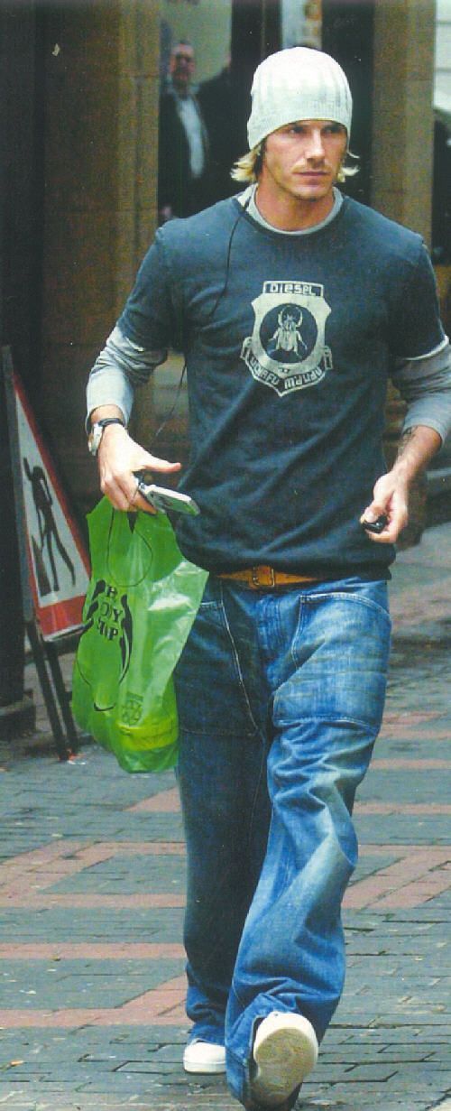 a man walking down the street with a green bag in his hand and wearing a beanie