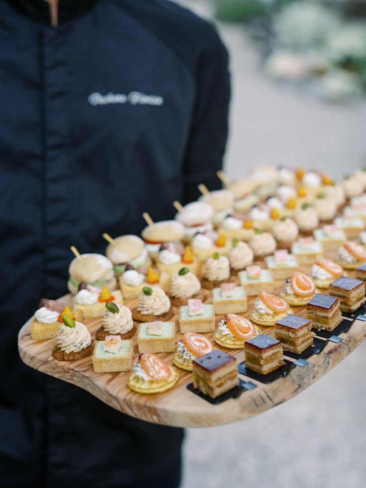 a man is holding a tray full of small sandwiches and pastries on sticks with toothpicks stuck in them