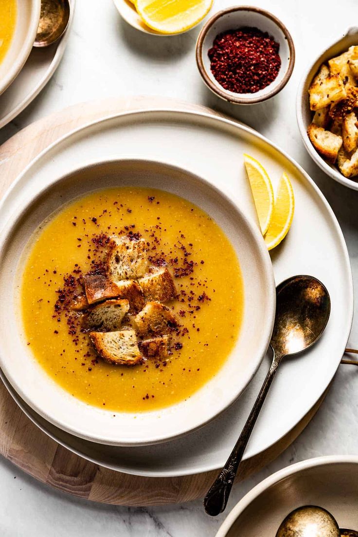 a white plate topped with soup next to bowls of bread and other foods on a table