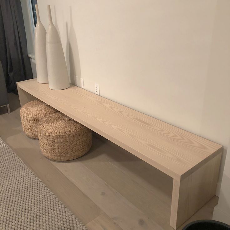 two white vases sitting on top of a wooden shelf next to a stool and ottoman