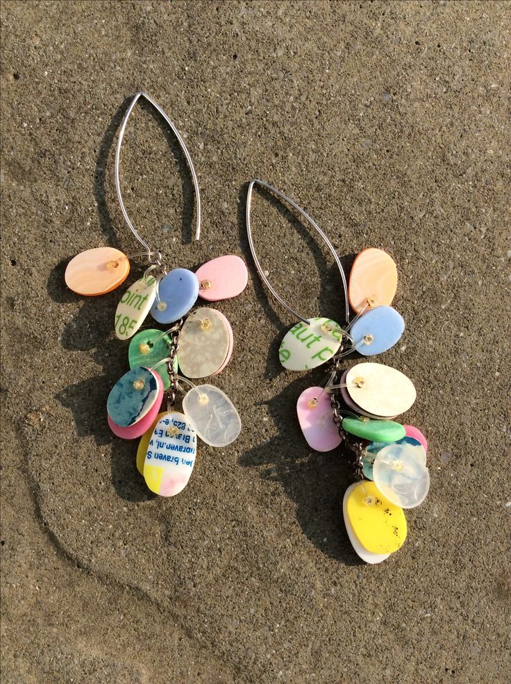 two pairs of earrings with buttons attached to them on the sand in front of water