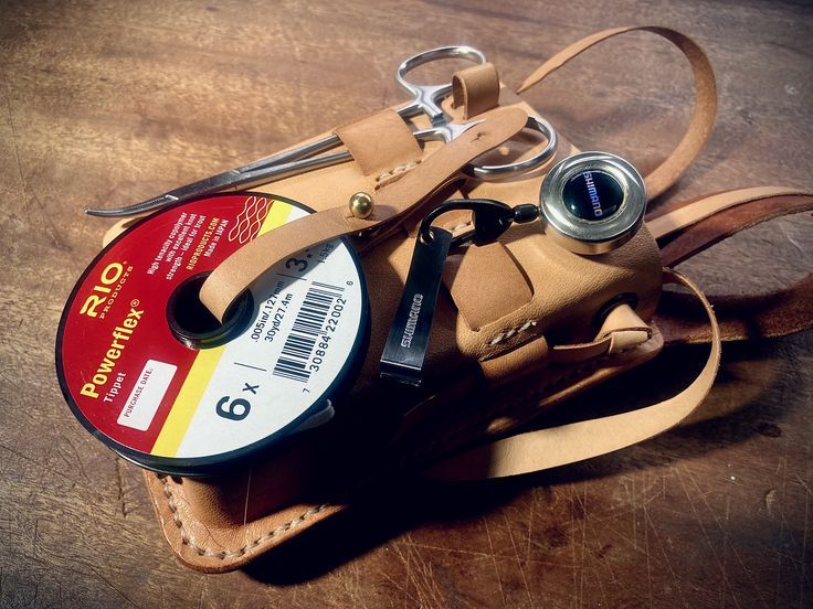 a brown leather case with a pair of scissors and a camera on it sitting on a wooden table