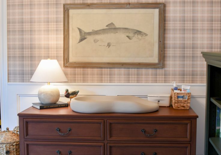 there is a fish painting on the wall above a dresser with drawers and lamps in front of it