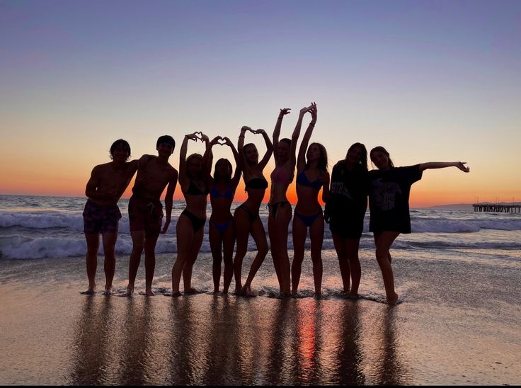 a group of people standing on top of a beach next to the ocean at sunset