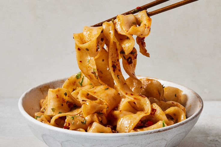 a bowl filled with noodles and chopsticks being lifted from the bowl by two chopsticks