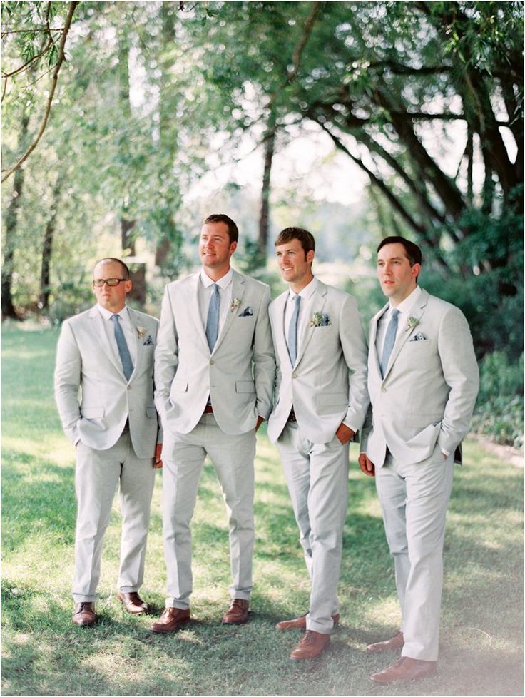 a group of men standing next to each other wearing suits and ties on grass covered ground