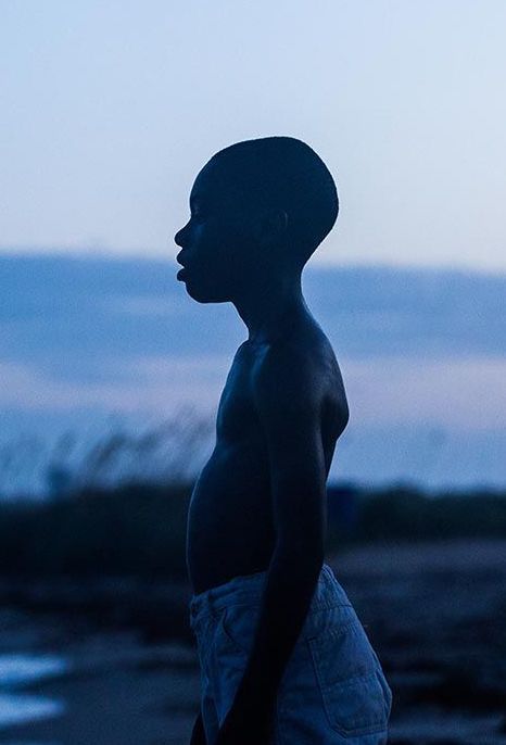 a young man standing in front of the ocean at dusk with his head turned to the side