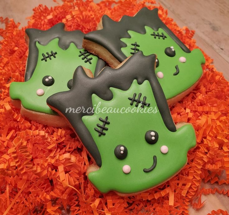 two decorated cookies sitting on top of orange shredded paper