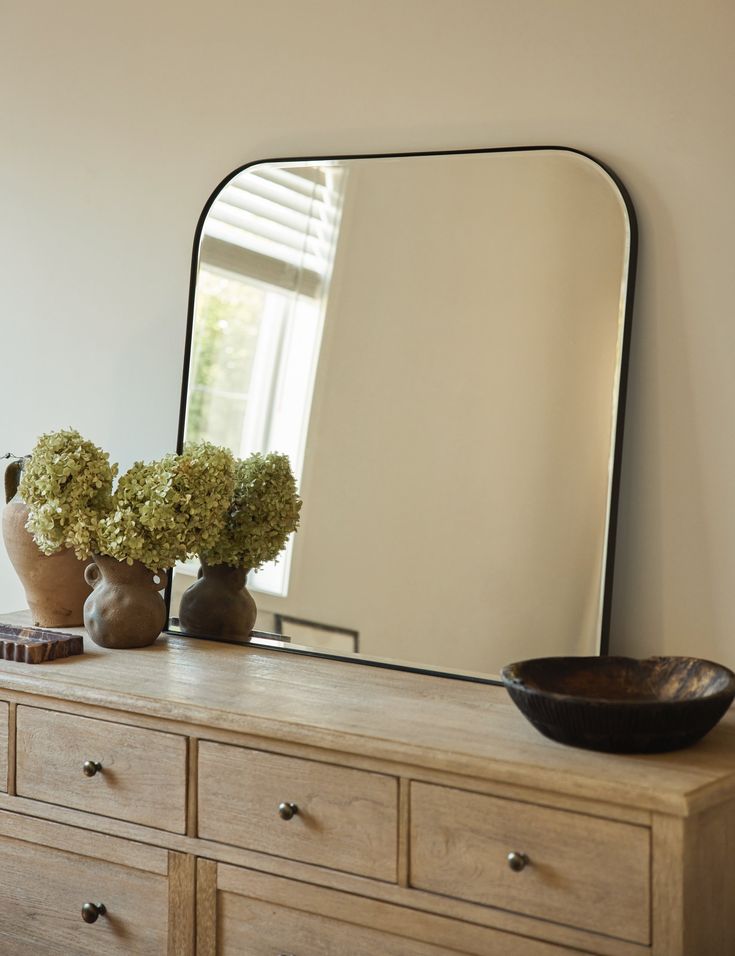 a large mirror sitting on top of a wooden dresser next to a vase filled with flowers