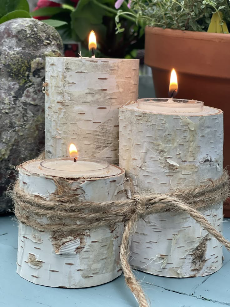 three white birch tree candles with twine and rope wrapped around them on a blue table