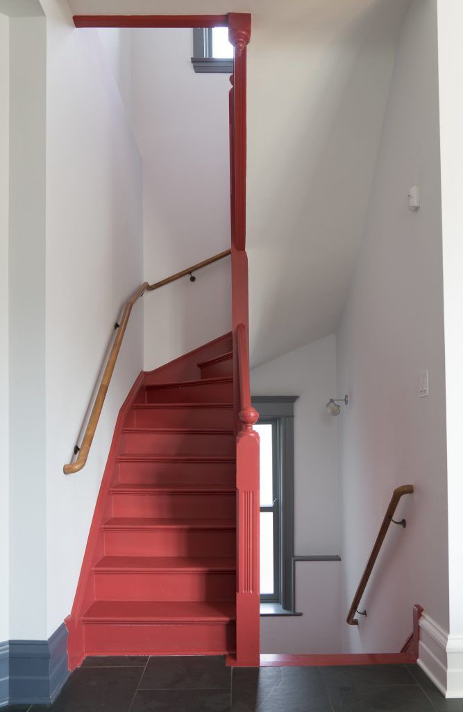 a red stair case next to a window in a white room with black tile flooring