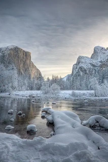 snow covered rocks and water in the middle of a mountain river with mountains in the background