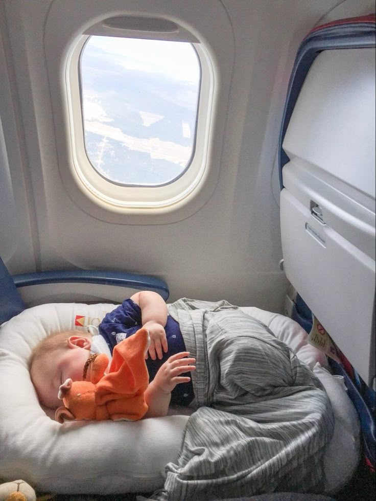 a small child laying on top of a pillow next to an airplane window