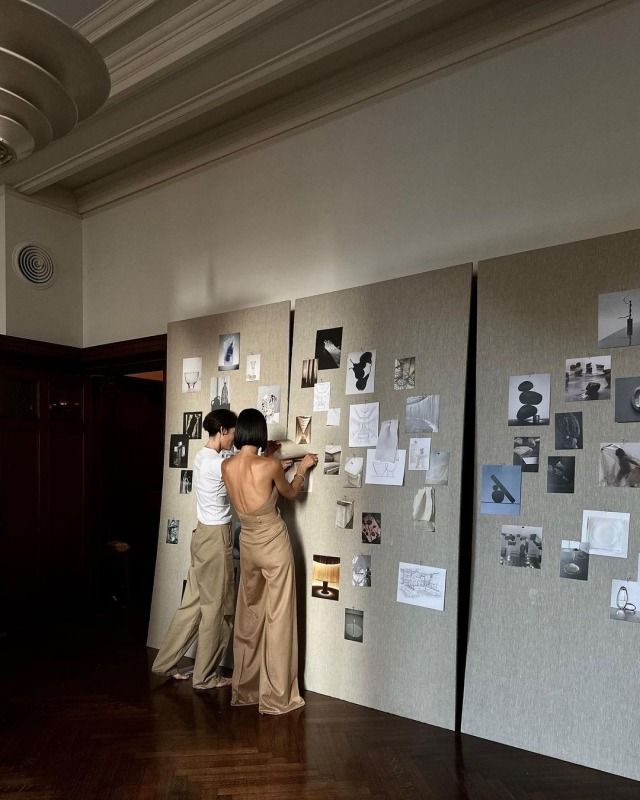 two people standing next to each other looking at pictures on the wall