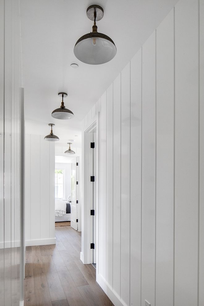 an empty hallway with white walls and wood flooring is seen in this image, there are three lights on either side of the door