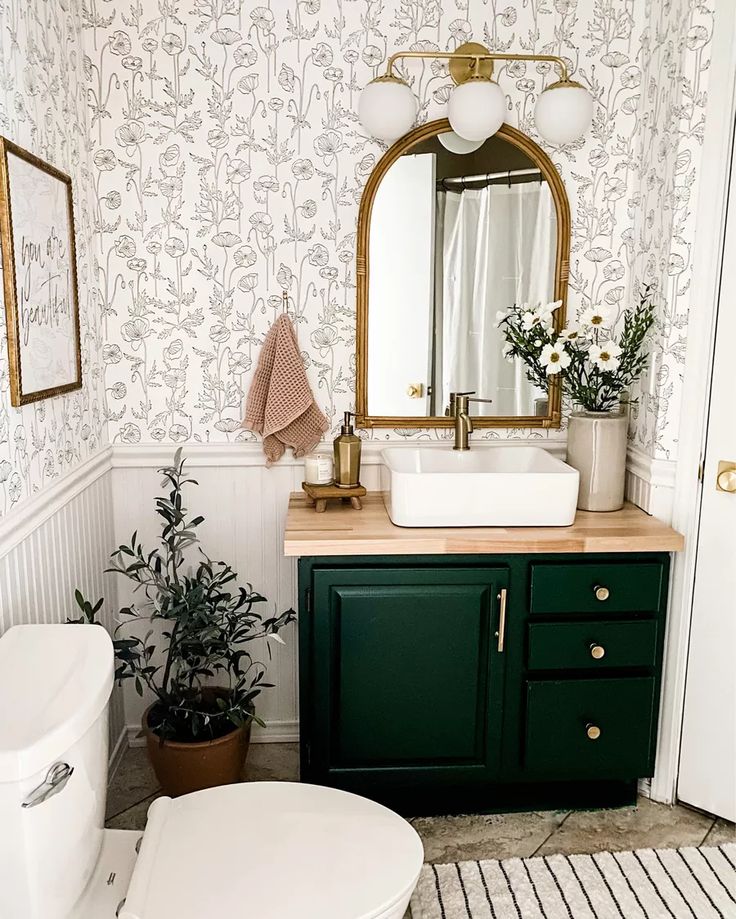 a white toilet sitting next to a bathroom sink under a mirror on top of a wooden counter