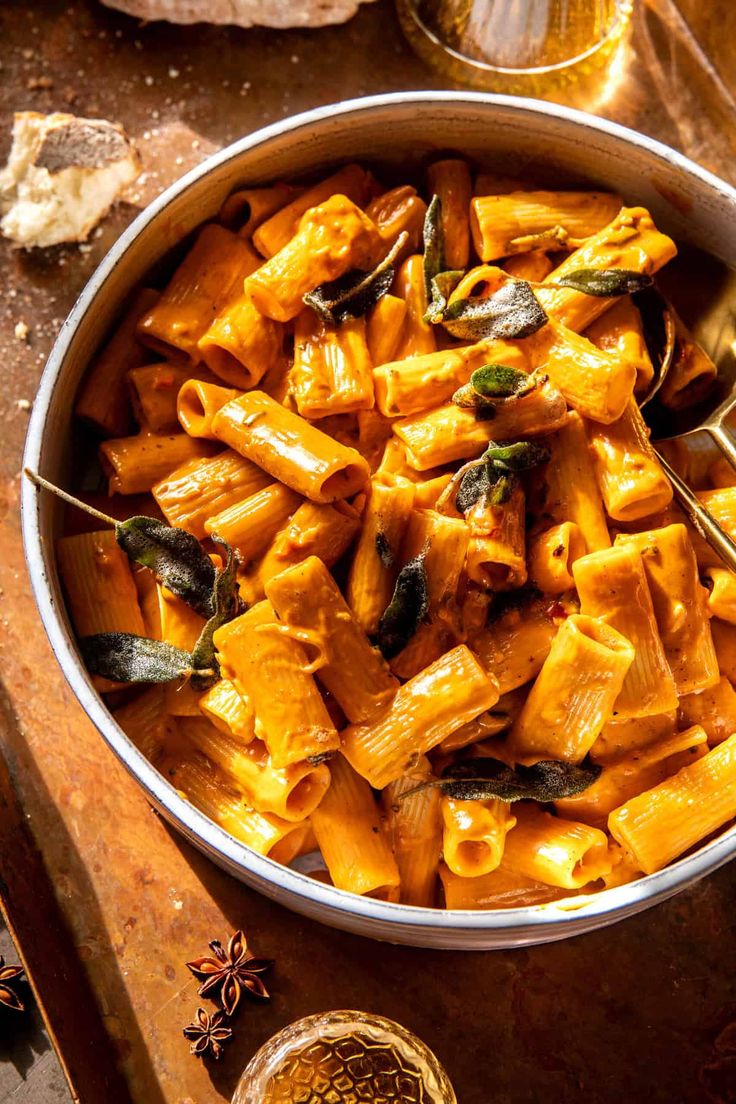 a bowl filled with pasta next to a glass of wine and some other food on a table