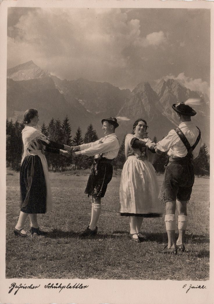 an old photo of four women standing in a field with mountains in the background and one woman holding out her arms