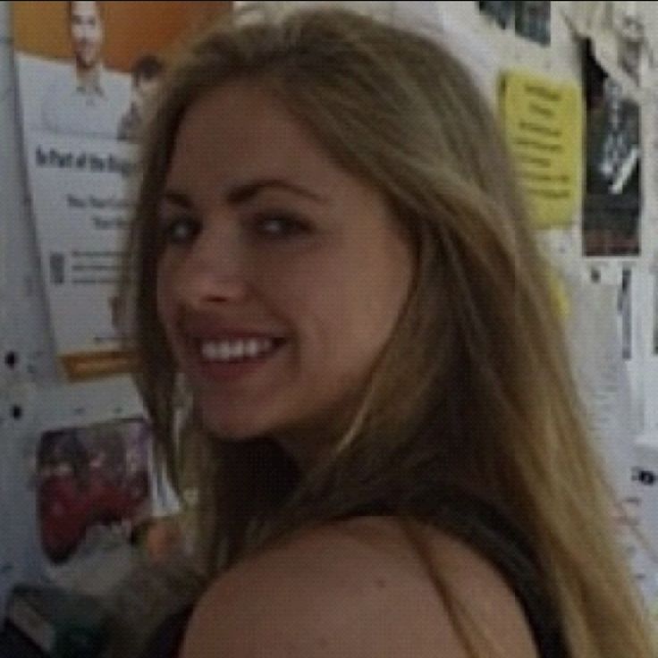 a woman with long blonde hair standing in front of a wall full of posters and papers