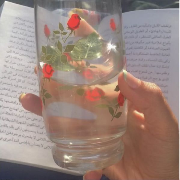 a person holding a glass with water and roses on it in front of an open book