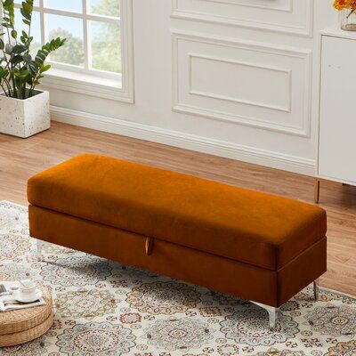 an orange bench sitting on top of a rug in a living room next to a potted plant