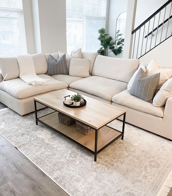 a living room with white couches and pillows on top of the rugs in front of two windows