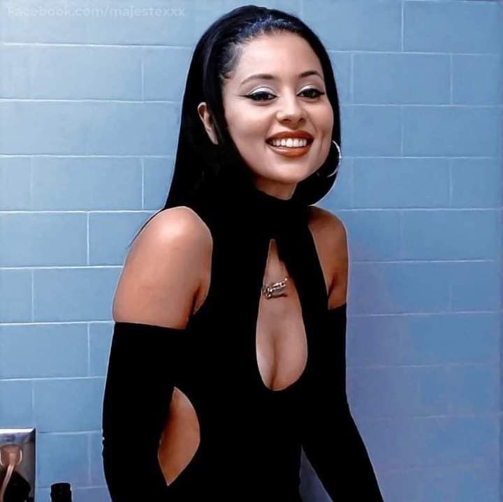 a woman in a black dress standing next to a blue tiled wall and smiling at the camera