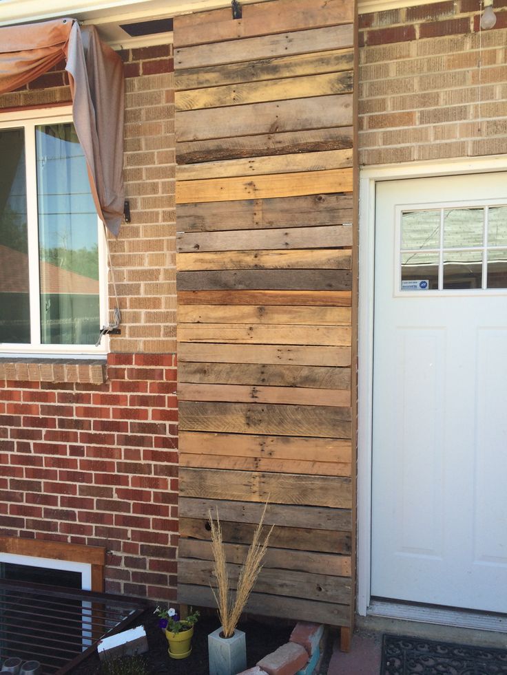 a wooden wall next to a white door in front of a brick building with two windows