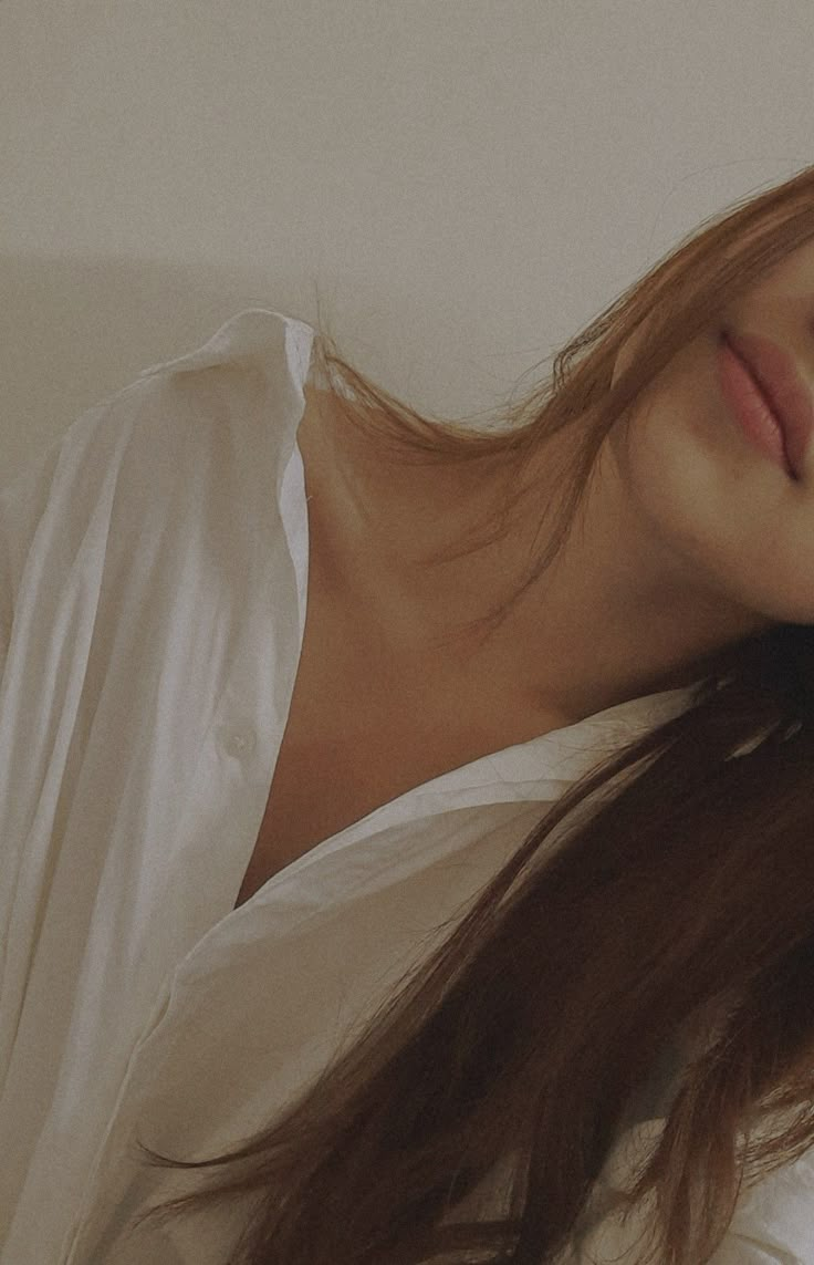 a woman with long brown hair laying on top of a white bed next to a wall