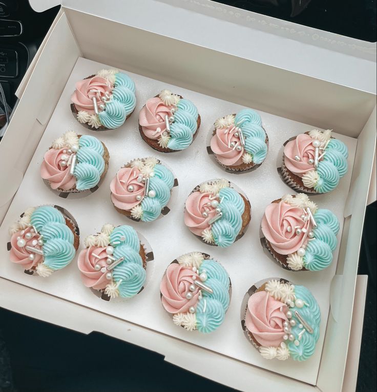 twelve cupcakes in a white box with pink and blue frosting