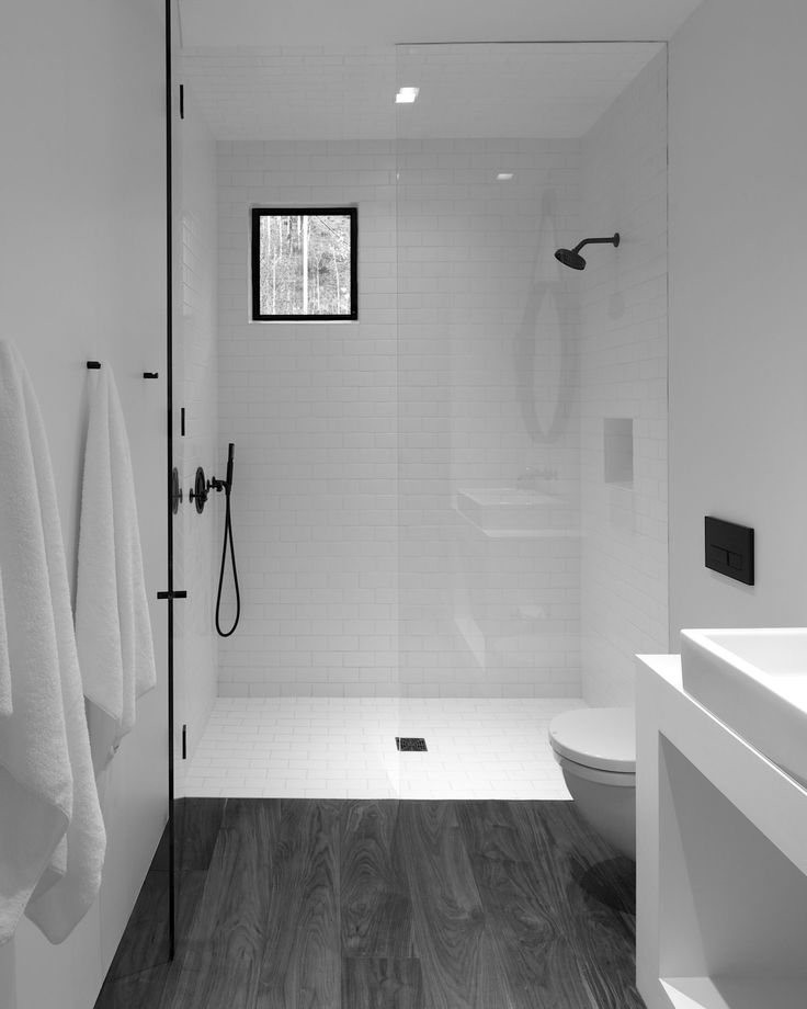 black and white photograph of a bathroom with wood flooring, glass shower door, and sink