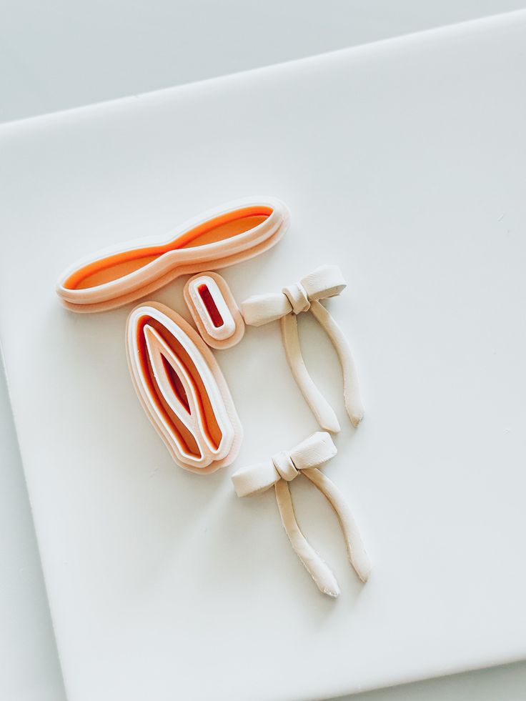 an orange and white pair of scissors sitting on top of a cutting board next to another pair of scissors