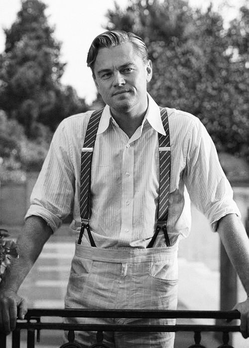 a man in suspenders leaning on a fence