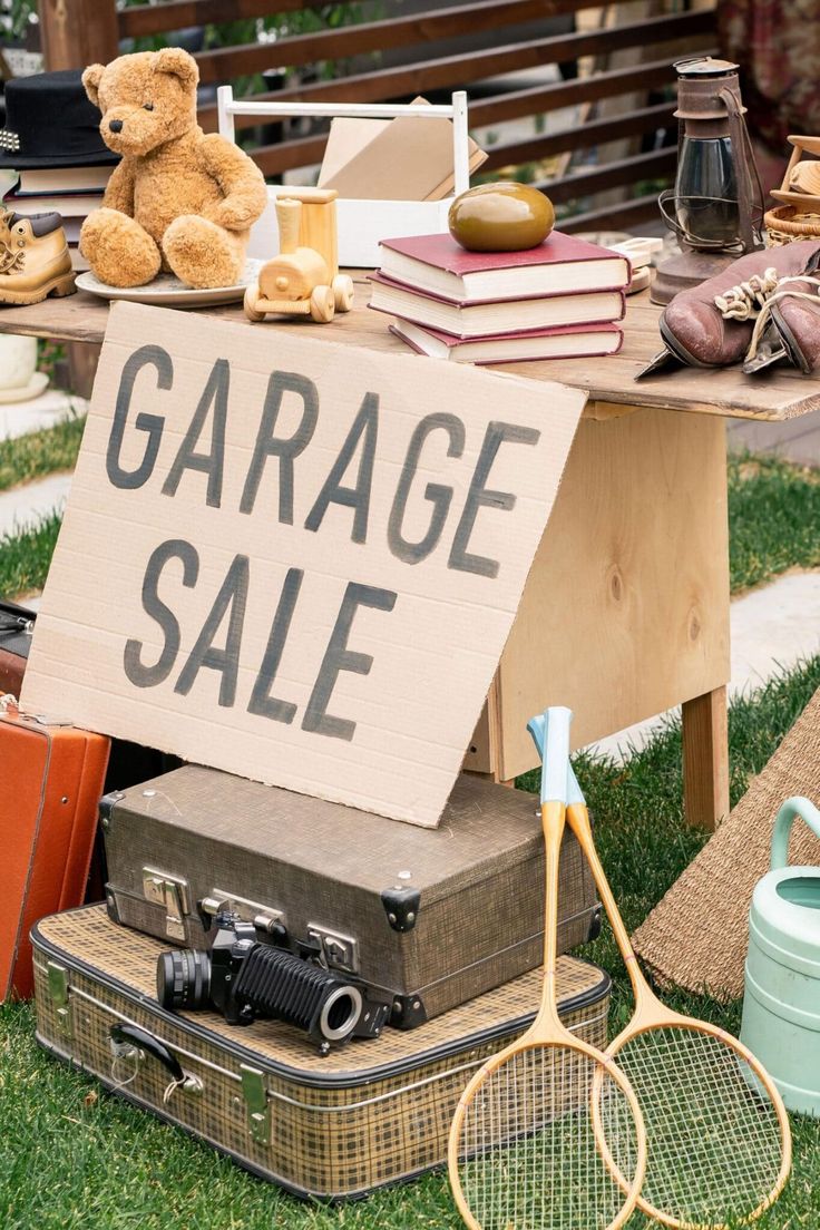 there is a sign that says garage sale next to old suitcases and tennis rackets