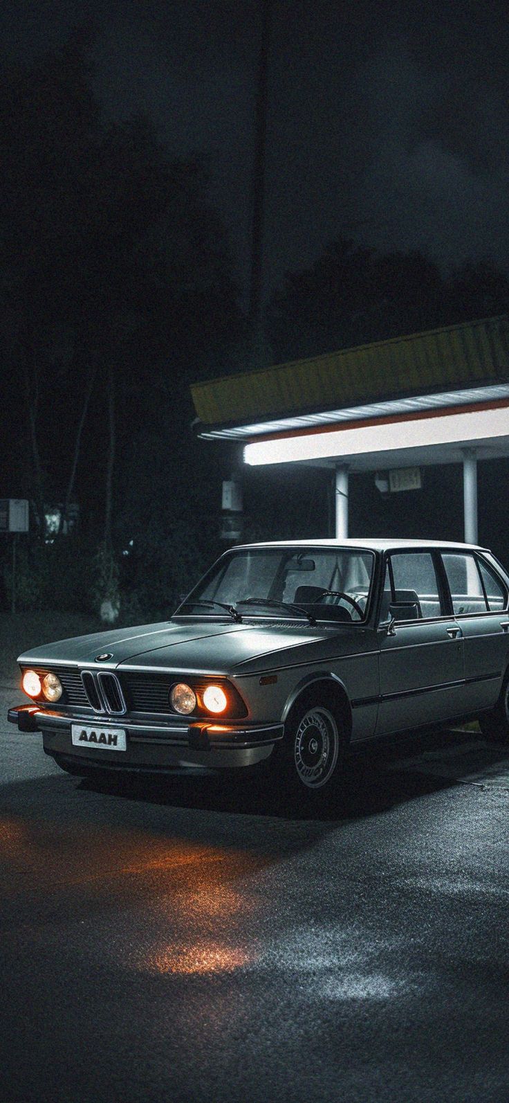 an old car is parked in front of a gas station at night with its lights on