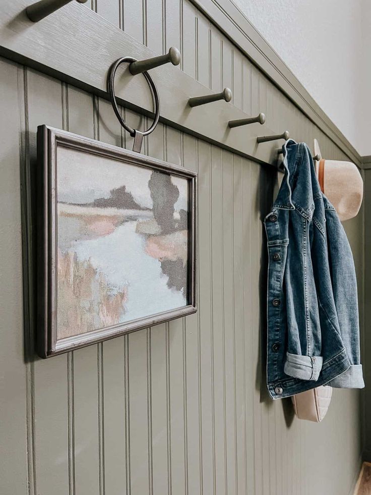 a pair of jeans hanging on the wall next to a coat rack and framed painting