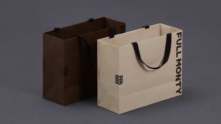 two brown and white shopping bags sitting side by side on a gray surface with black handles