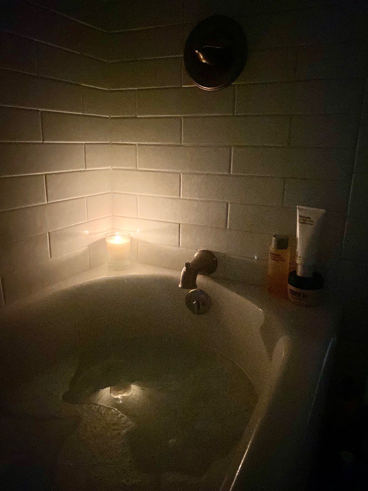 a bathtub with soap and lotion on it in the dark, lit by a candle